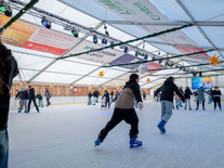Große Eisfläche mit vielen Schlittschuhläufern unter Sternen, Spiegelkugel und winterlicher Beleuchtung