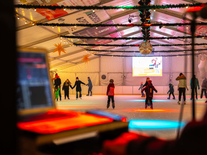 Blick auf die Eisbahn mit bunten Lichtern, winterlicher Dekoration und mehreren Schlittschuhläufern