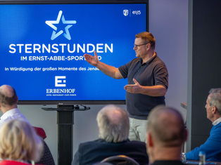 Redner vor einem Bildschirm mit dem Logo der Sternstunden im Ernst-Abbe-Sportfeld