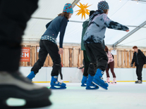 Kinder und Jugendliche fahren auf der Eisbahn unter Stern, Lichterkette und Winterdekoration