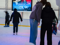 Besucher fahren Schlittschuh vor einer großen Leinwand in der überdachten Eiswelt Jena
