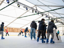 Kinder üben mit Eislaufhilfen auf der Eisbahn unter Stern, Spiegelkugel und Winterbeleuchtung