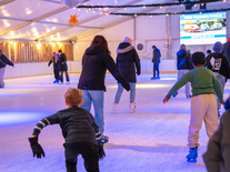 Kinder und Erwachsene laufen unter Lichterketten auf der überdachten Eisbahn