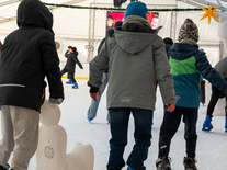 Kinder und Jugendliche fahren mit einer Eislaufhilfe über die Eisfläche unter winterlicher Dekoration