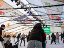 Kinder und Jugendliche nutzen Eislaufhilfen auf der Eisbahn unter festlicher Beleuchtung