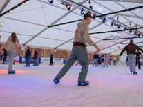 Jugendliche und Erwachsene fahren unter Sternen, Spiegelkugel und Lichterketten über die Eisfläche