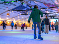 Besucher auf der überdachten Eisbahn unter Lichterketten und winterlicher Dekoration