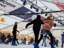 Kinder und Erwachsene nutzen die Eisbahn mit Lernhilfen unter winterlicher Beleuchtung