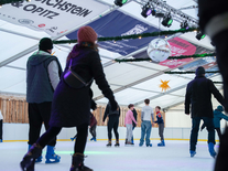 Besucher auf Schlittschuhen unter Spiegelkugel, Sternen und farbiger Beleuchtung auf der Eisbahn