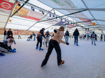 Viele Besucher fahren und üben auf der Eisfläche unter winterlicher Dekoration und bunter Beleuchtung
